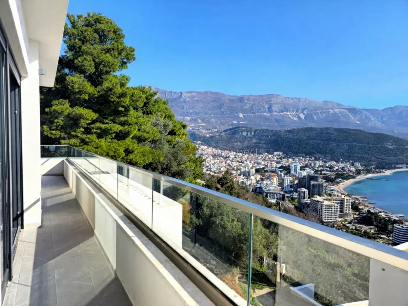 Panoramablick auf das Meer und Budva vom großzügigen Balkon einer modernen Villa in Montenegro mit Glasgeländer.