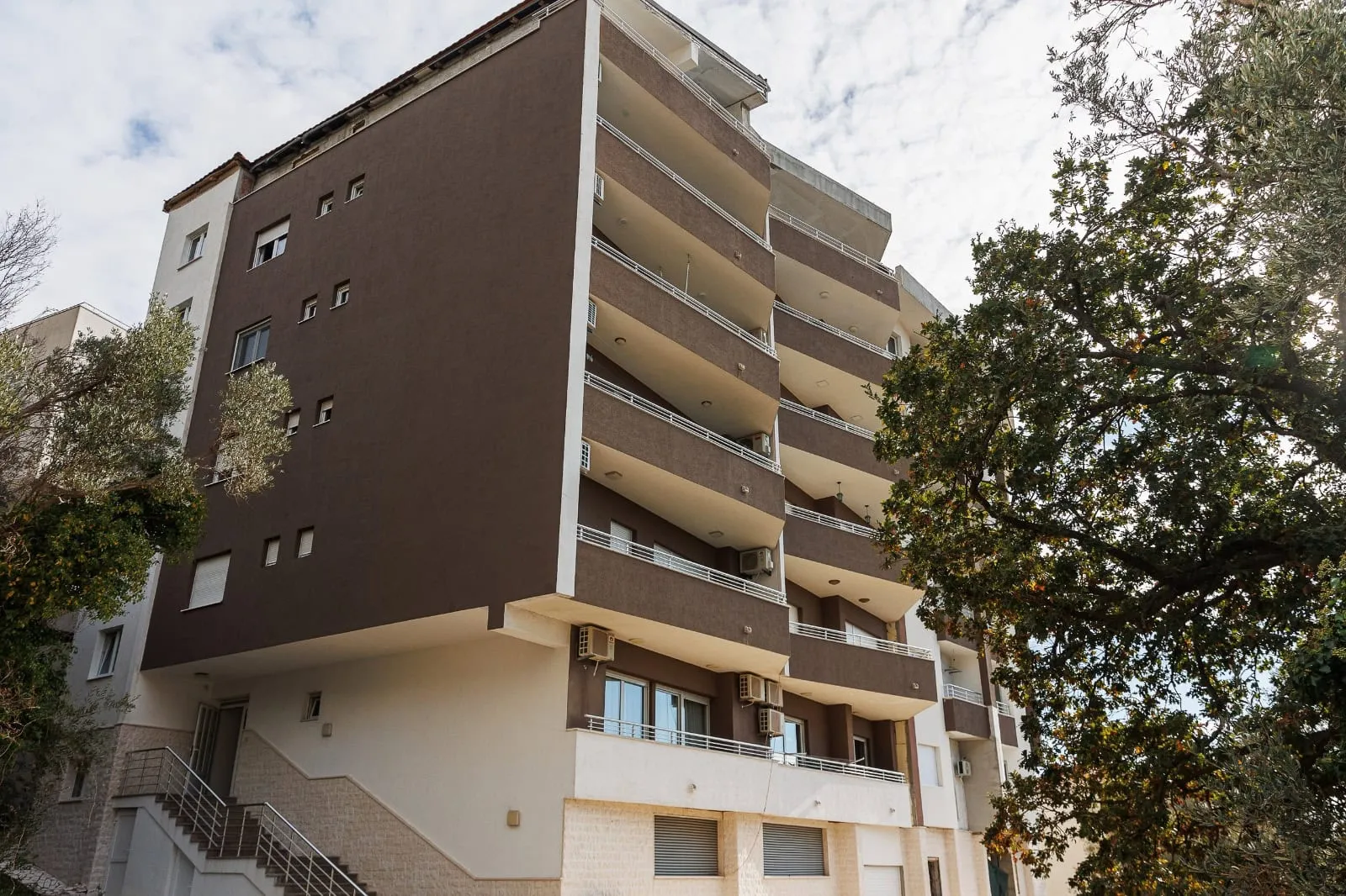 Vue extérieure d'un immeuble de plusieurs étages avec balcons, escalier extérieur et arbres environnants.