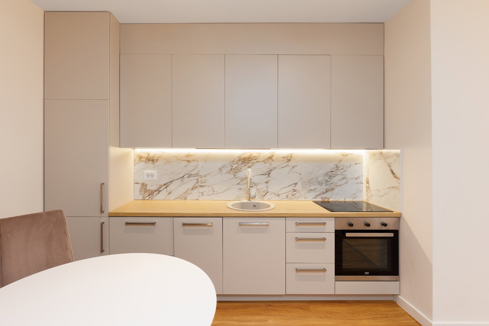Moderne Küche mit beigen Fronten, Marmor-Rückwand und Geräten in einer Wohnung in Bečići, Montenegro