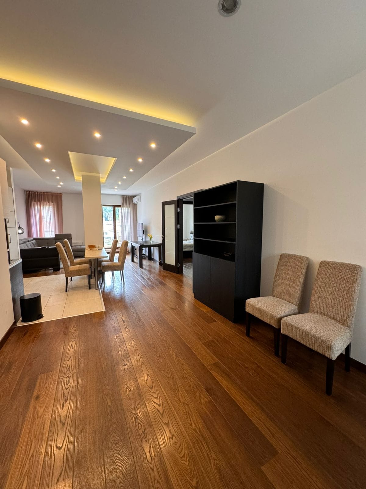 Geräumiges Wohnzimmer in einer Wohnung in Budva, Montenegro: Holzboden, moderne Beleuchtung und Essbereich.