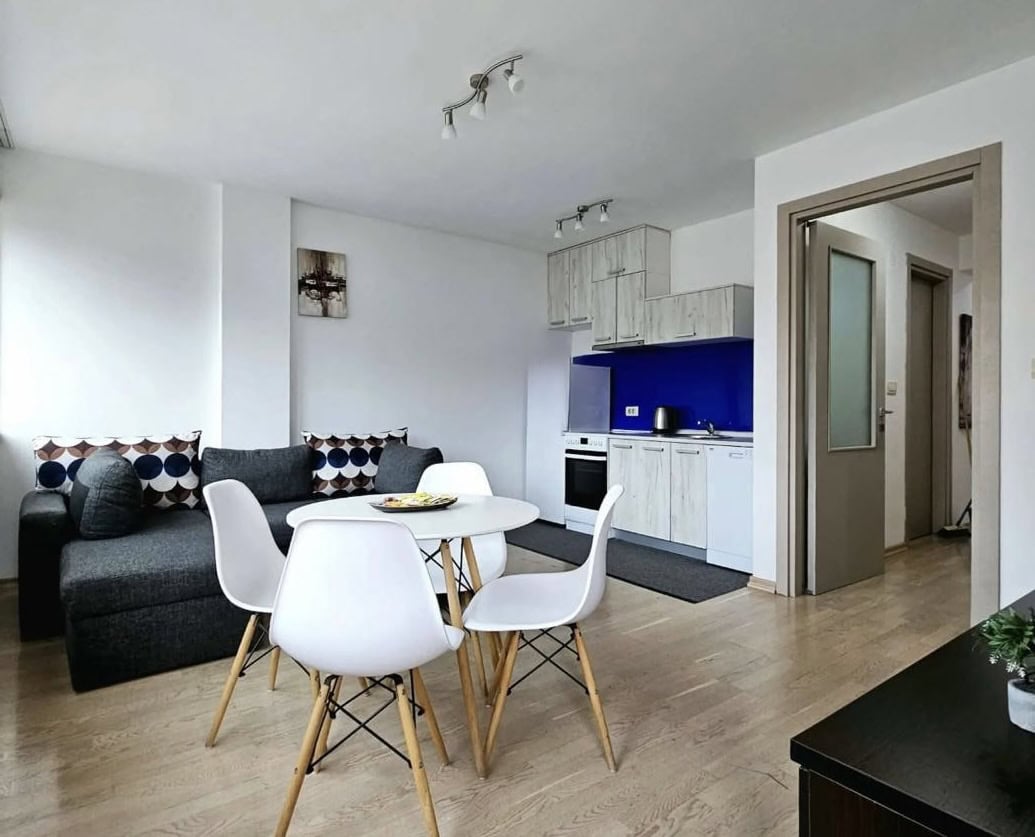 Modern living room with kitchen in an apartment in Becici, Budva, Montenegro: gray sofa, dining area, and light-colored furniture.
