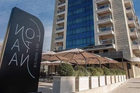 Facade of the modern Fontan residential complex in Bečići, Budva, Montenegro, with the restaurant summer terrace and umbrellas.