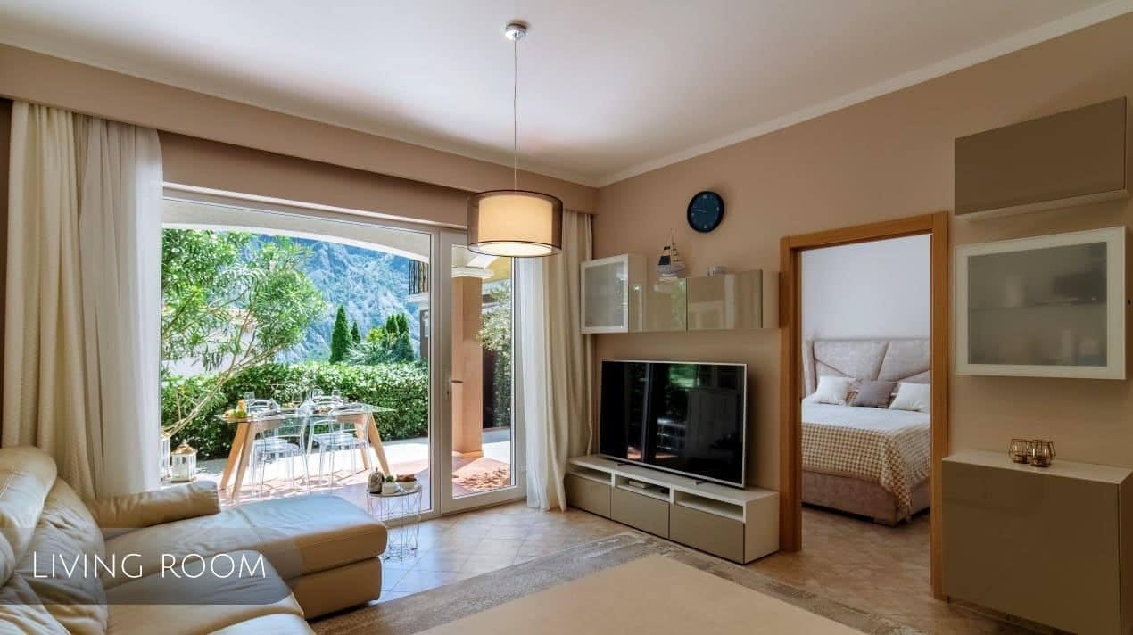 Svetao dnevni boravak u stanu, Orahovac, Crna Gora: savremeni nameštaj, TV zona i izlaz na terasu s pogledom na planine.