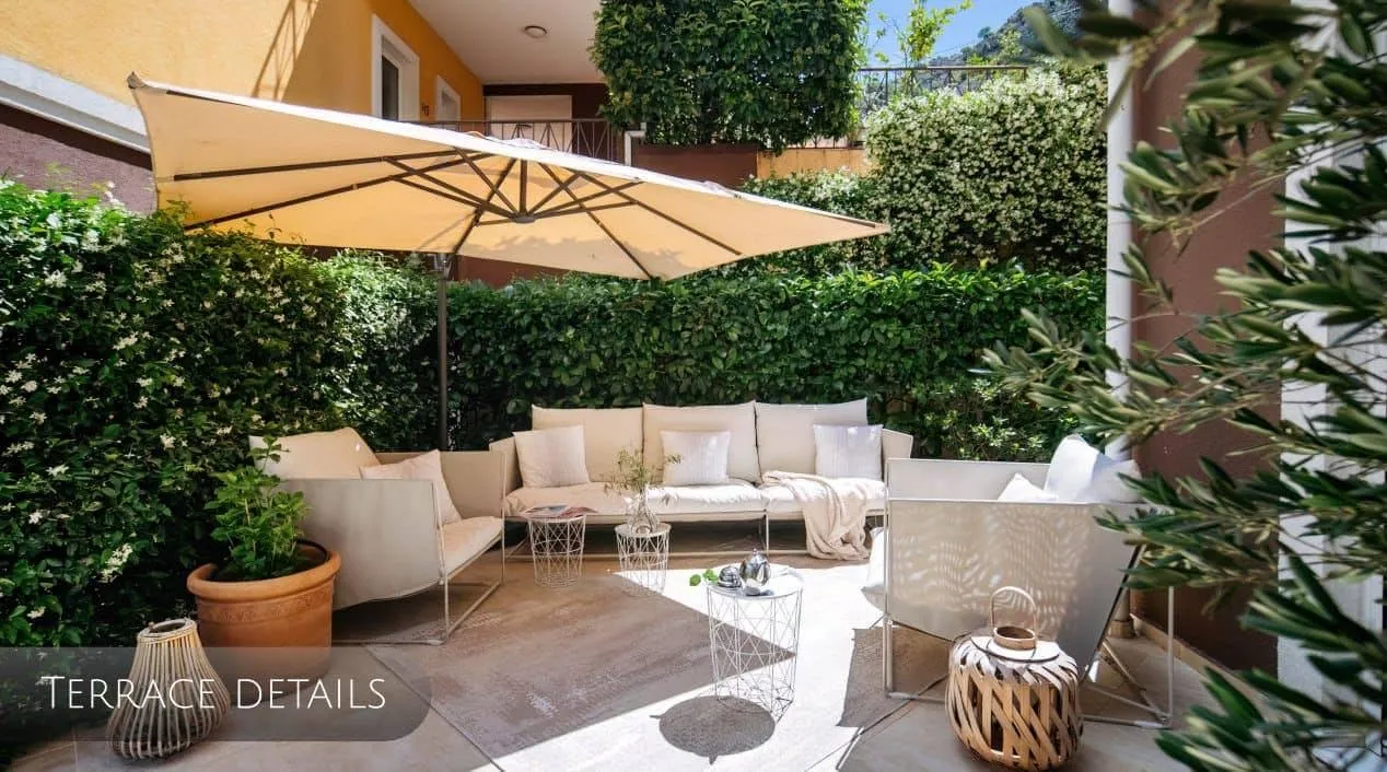 Cozy terrace with garden furniture and an umbrella in an apartment in Orahovac, Montenegro, surrounded by a hedge.