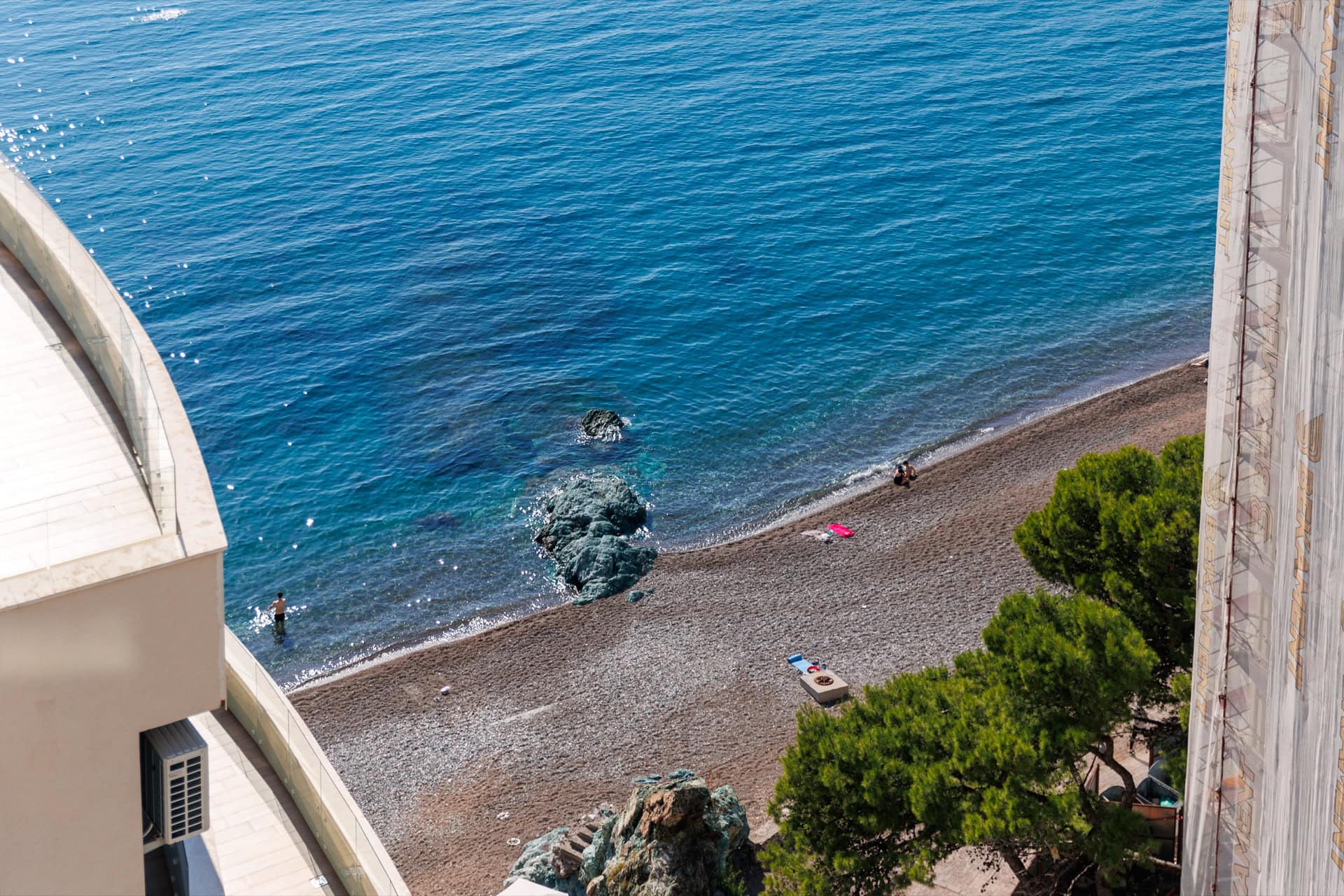 Blick vom Balkon der Wohnung in Bečići, Montenegro: Panorama auf einen privaten Kiesstrand und das azurblaue Adriatische Meer.