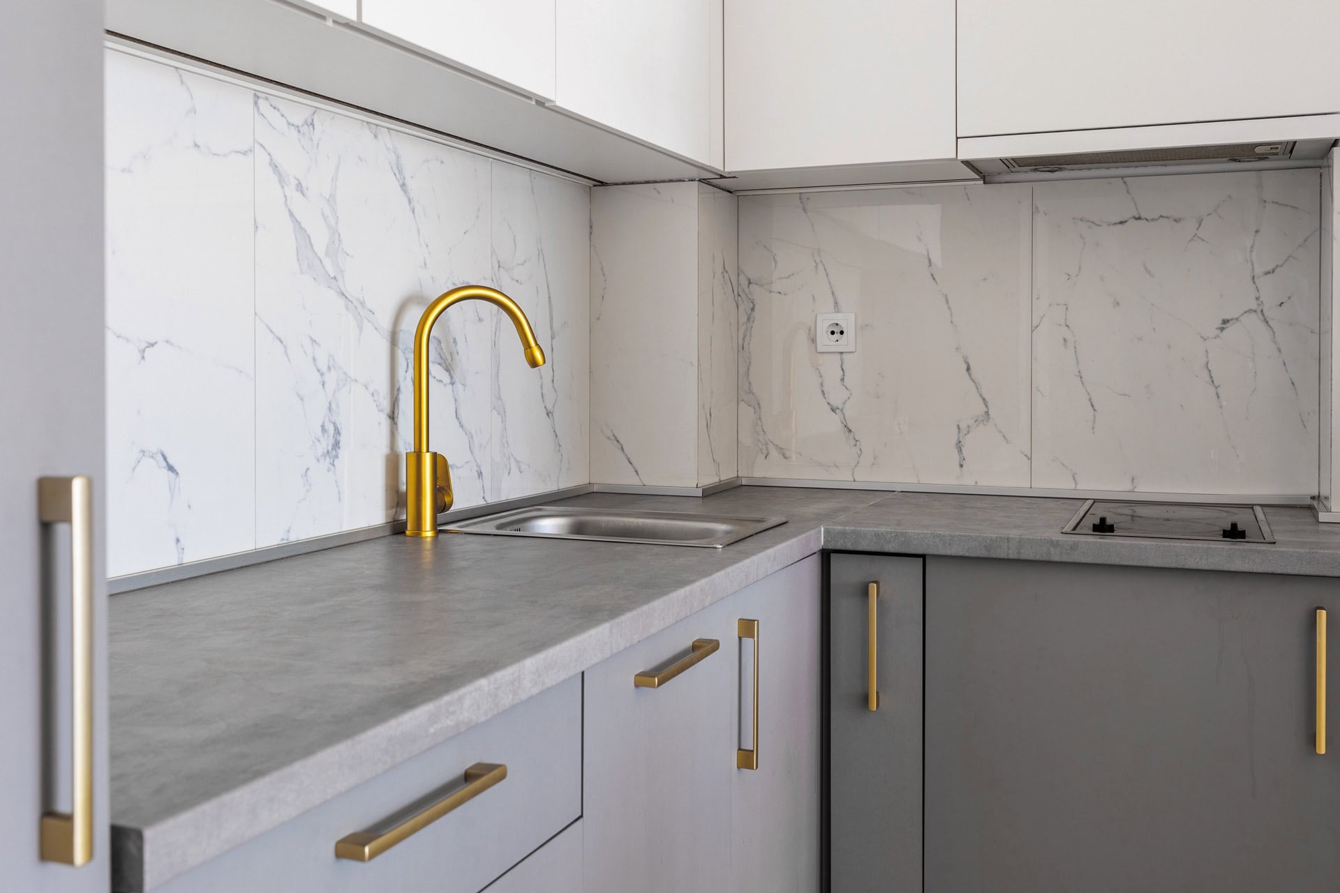 Moderne Küche in einer Wohnung in Bečići, Montenegro: graue Fronten, goldener Wasserhahn und Spritzschutz in weißer Marmoroptik.