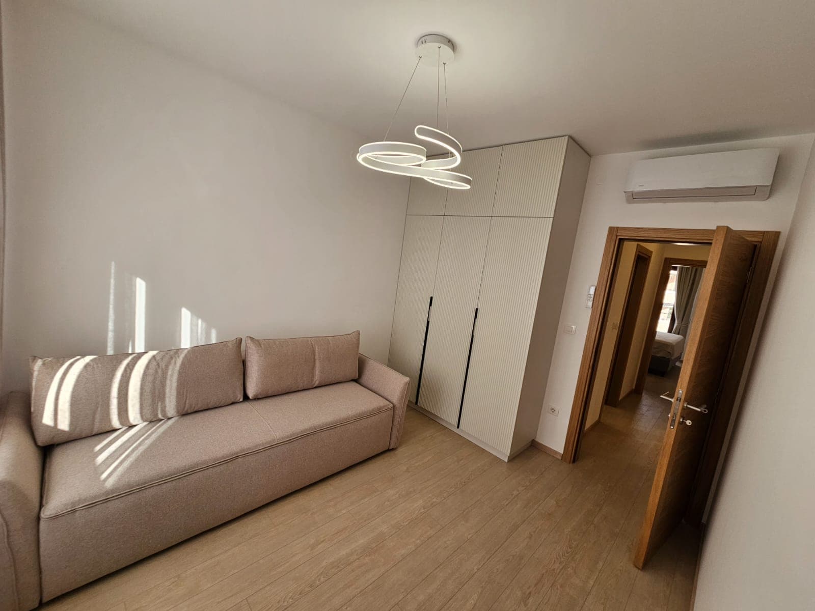 Savremena dnevna soba u stanu u Budvi, Crna Gora: bež sofa, ugradni ormar, dizajnerski luster i klima uređaj.