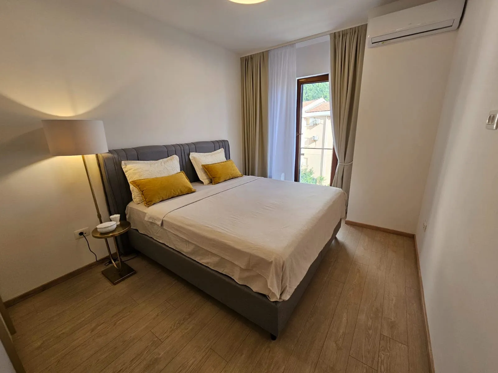 Gemütliches Schlafzimmer mit Doppelbett in einer Wohnung in Budva, Montenegro: helles Interieur, Laminatboden und Klimaanlage.