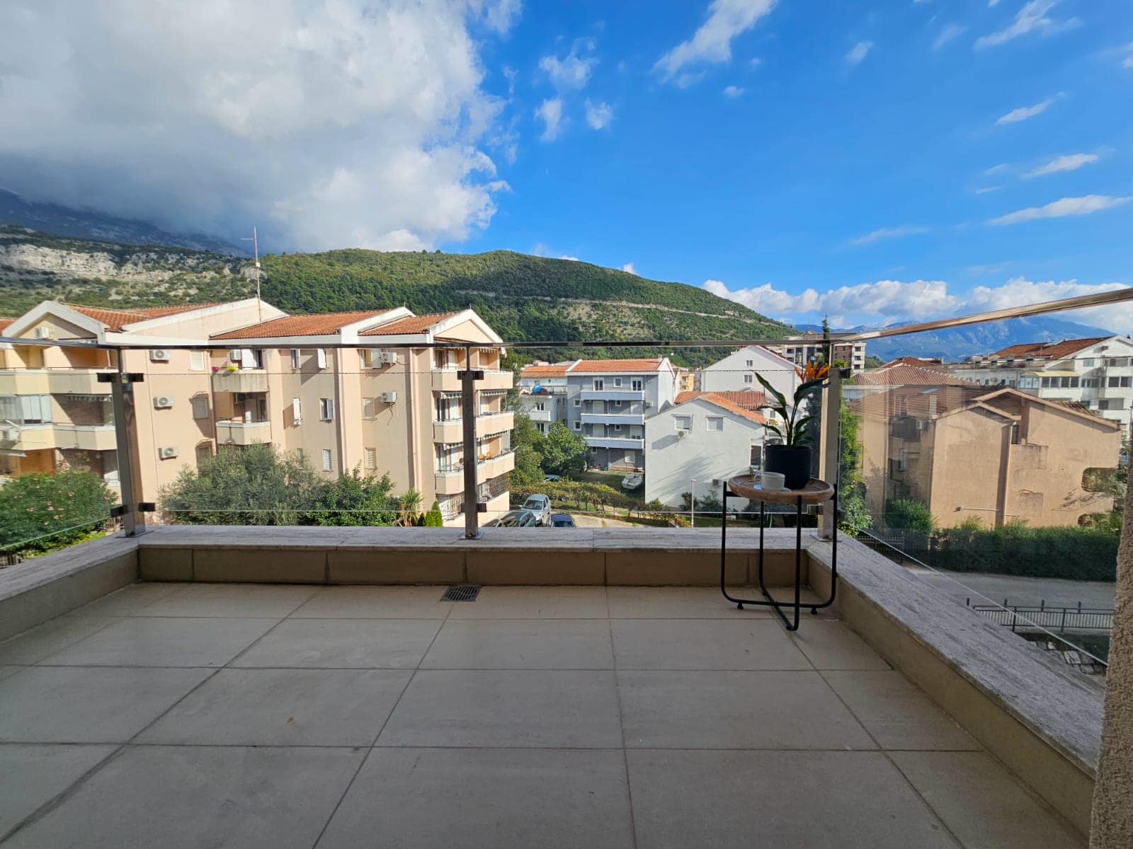 Prostran balkon s panoramskim pogledom na planine i grad u stanu, Budva, Crna Gora, sa stočićem za kafu i ogradom.