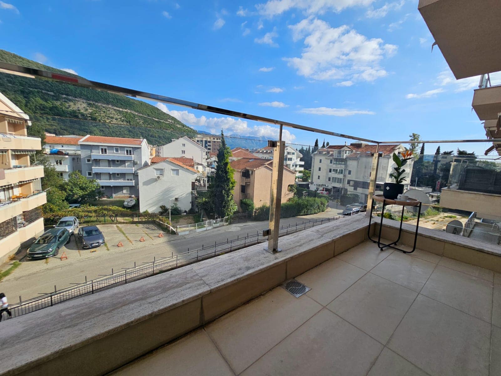 Prostran balkon s panoramskim pogledom na planine i grad Budvu, Crna Gora, sa modernom staklenom oblogom ograde.