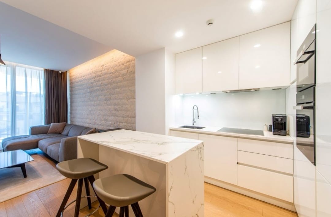 Modern kitchen-living room with a marble island in an apartment in Budva, Montenegro: white furniture and a stylish interior.