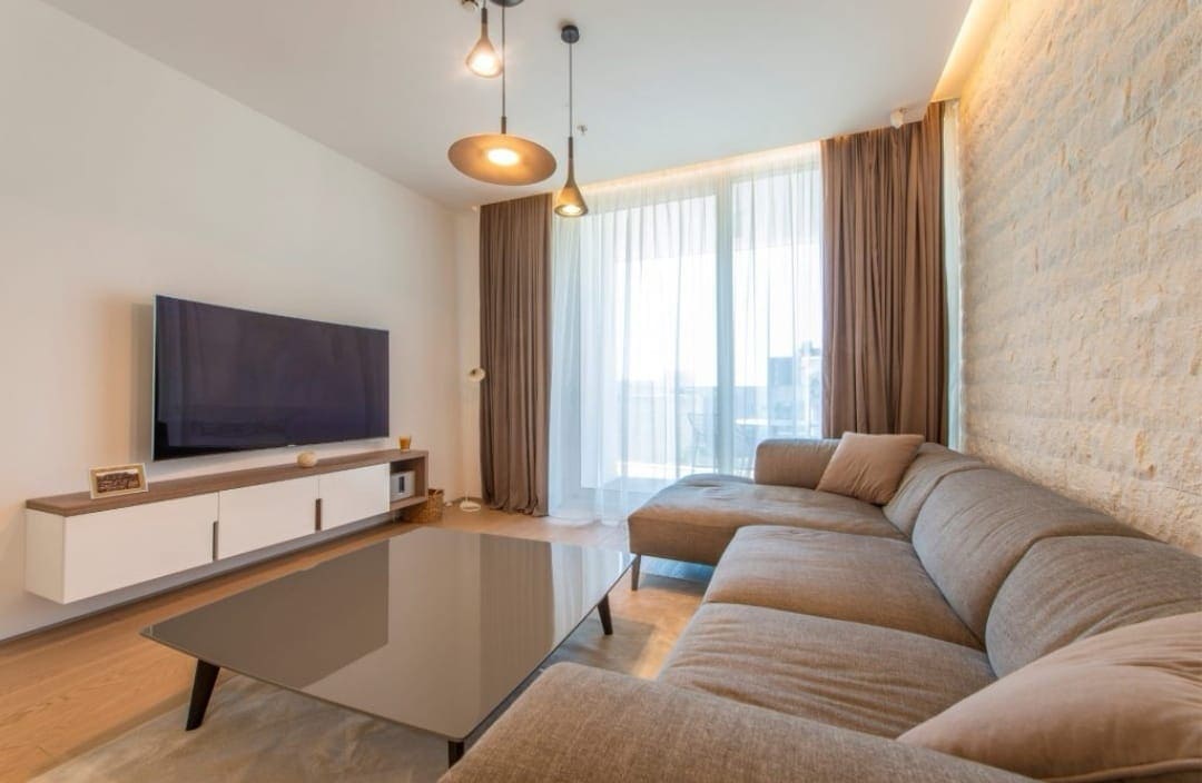 Modern living room in an apartment in Budva, Montenegro: corner sofa, TV area, and a wall finished with decorative stone.