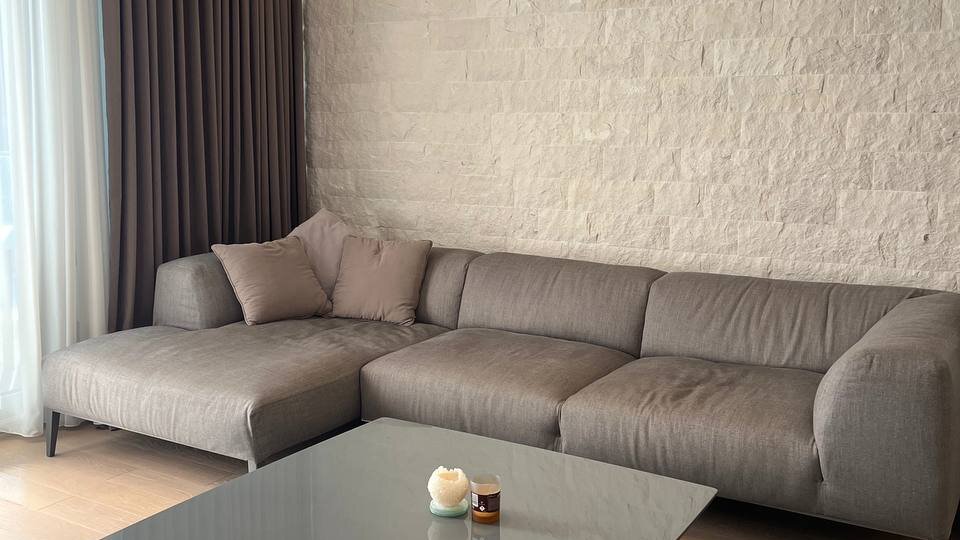 Living room in an apartment in Budva, Montenegro: gray corner sofa, coffee table, and a natural stone wall.