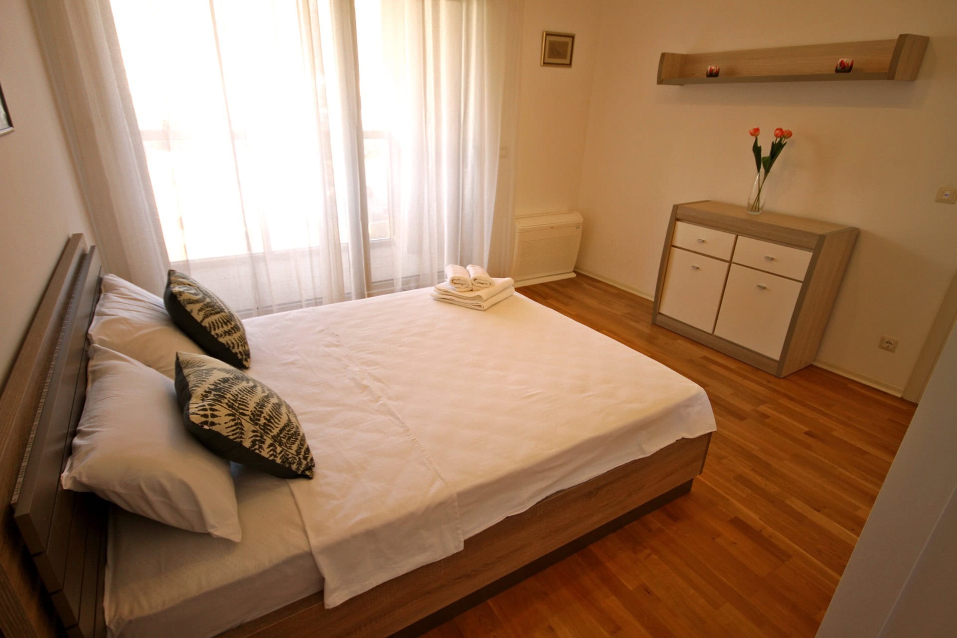 Gemütliches Schlafzimmer mit Doppelbett und Parkett in einer Wohnung in Budva, Montenegro. Helles Interieur mit Kommode.