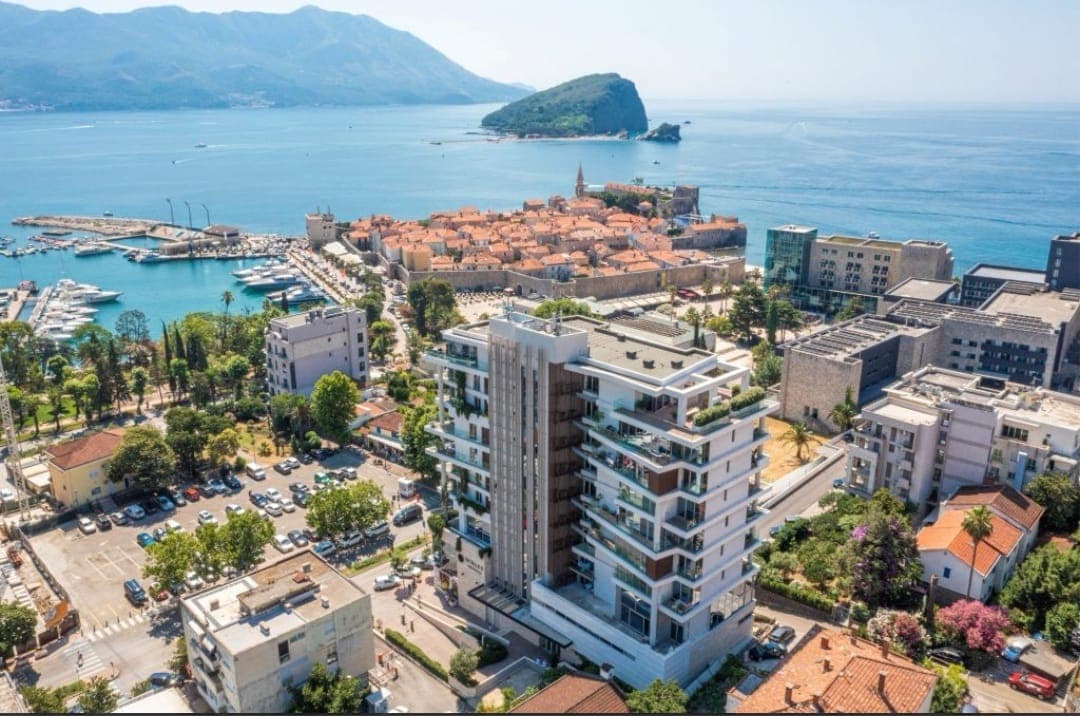 Aerial view of a modern residential complex in Budva, Montenegro, with a panorama of the Old Town, marina, and sea.