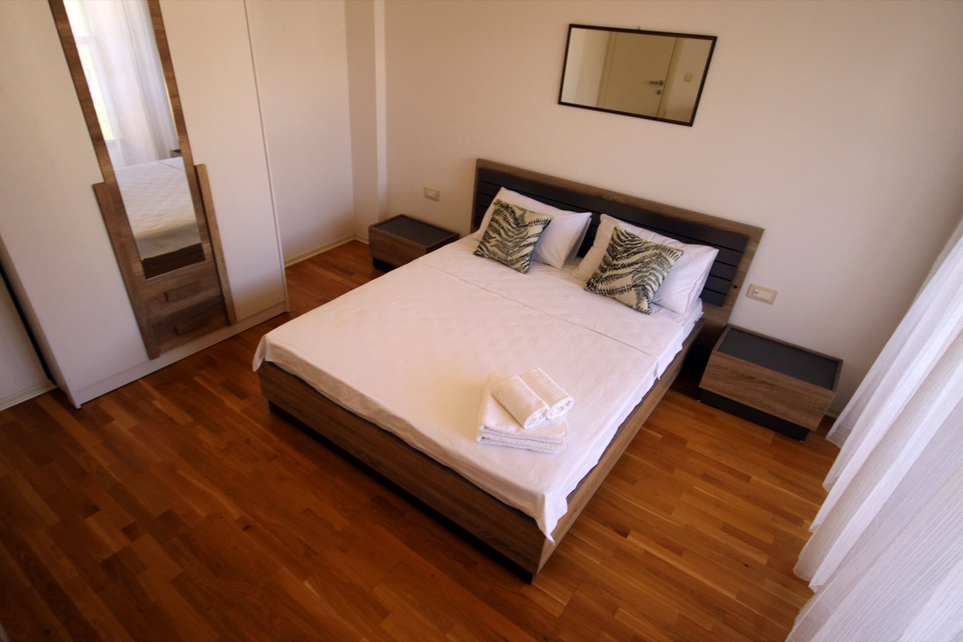 Schlafzimmer in einer Wohnung in Budva, Montenegro: Doppelbett, Holzboden, Kleiderschrank mit Spiegel und helles Interieur.