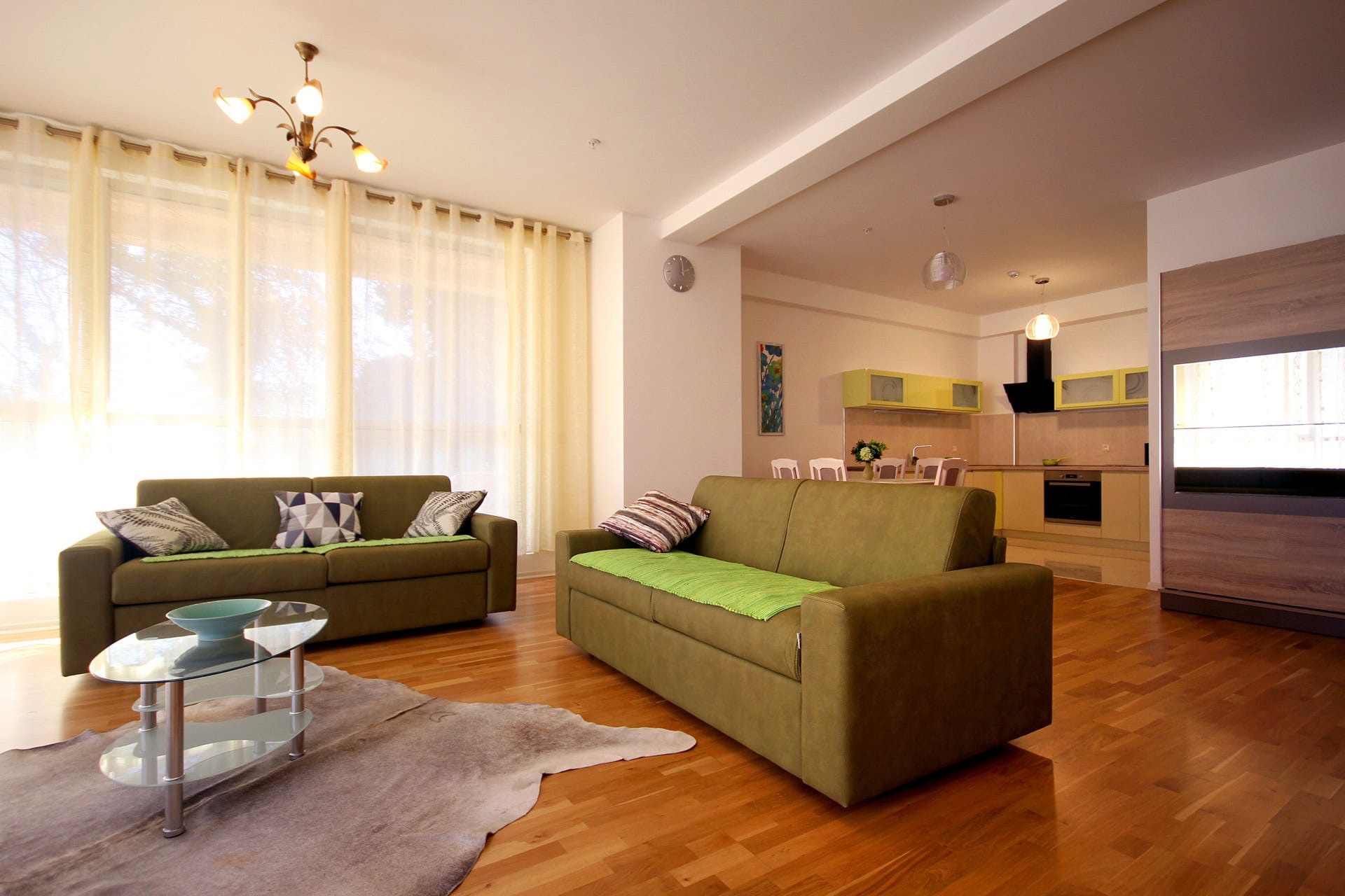 Geräumiges Wohnzimmer mit Küche in einer Wohnung in Budva, Montenegro: zwei grüne Sofas, Parkett und moderne Möbel.