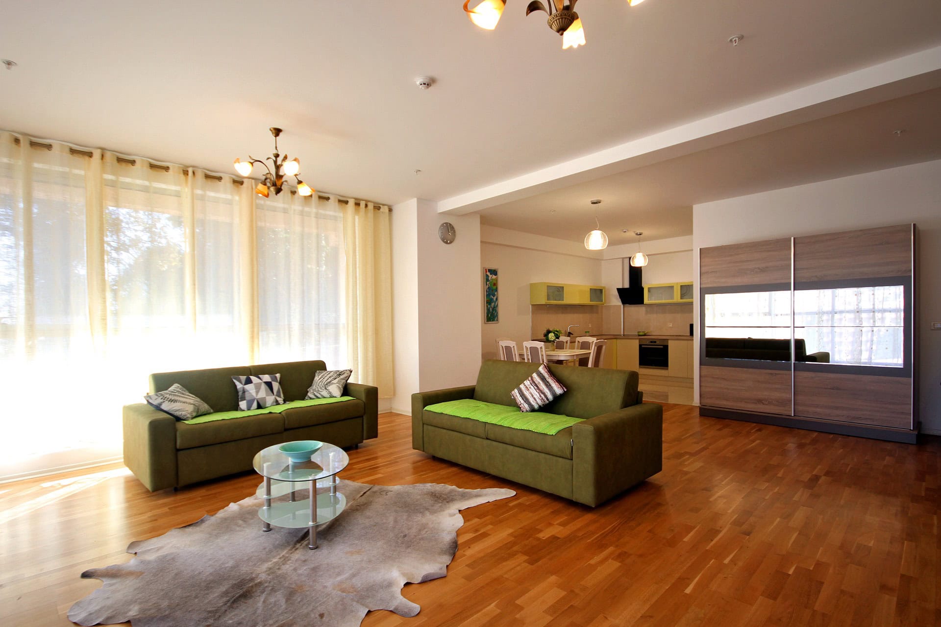 Geräumiges Wohnzimmer mit grünen Sofas und Küche in einer Wohnung in Budva, Montenegro: modernes Interieur, Parkettboden.