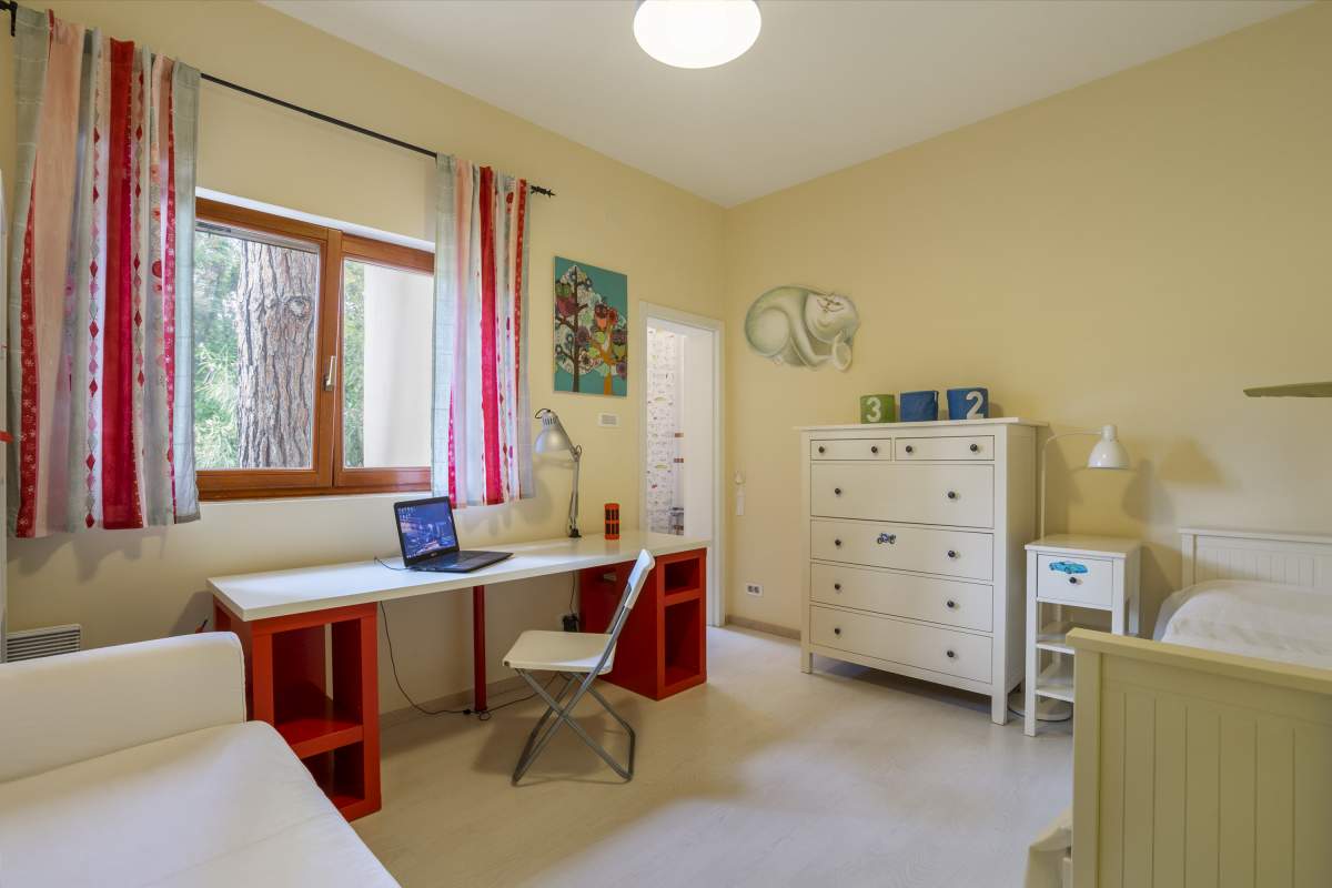 Helles Kinderzimmer in einer Villa in Bigovo, Montenegro: Schreibtisch, Kommode, Bett und Blick auf den Kiefernwald.