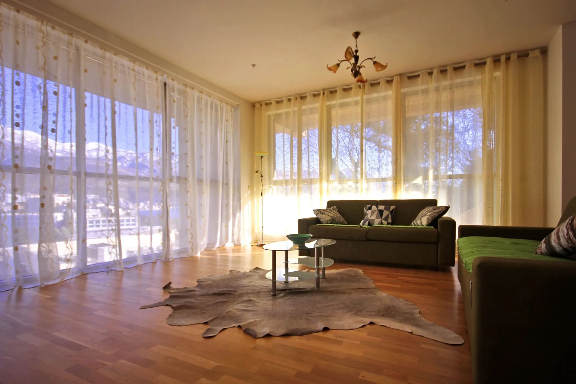 Jasny salon w mieszkaniu w Budvie, Czarnogóra: panoramiczne okna, widok na góry, miękkie meble i parkiet.