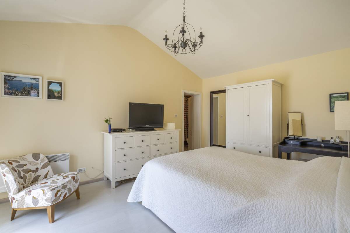 Gemütliches Schlafzimmer mit weißen Möbeln und hoher Decke in einer Villa in Bigovo, Montenegro: Doppelbett und Sessel.