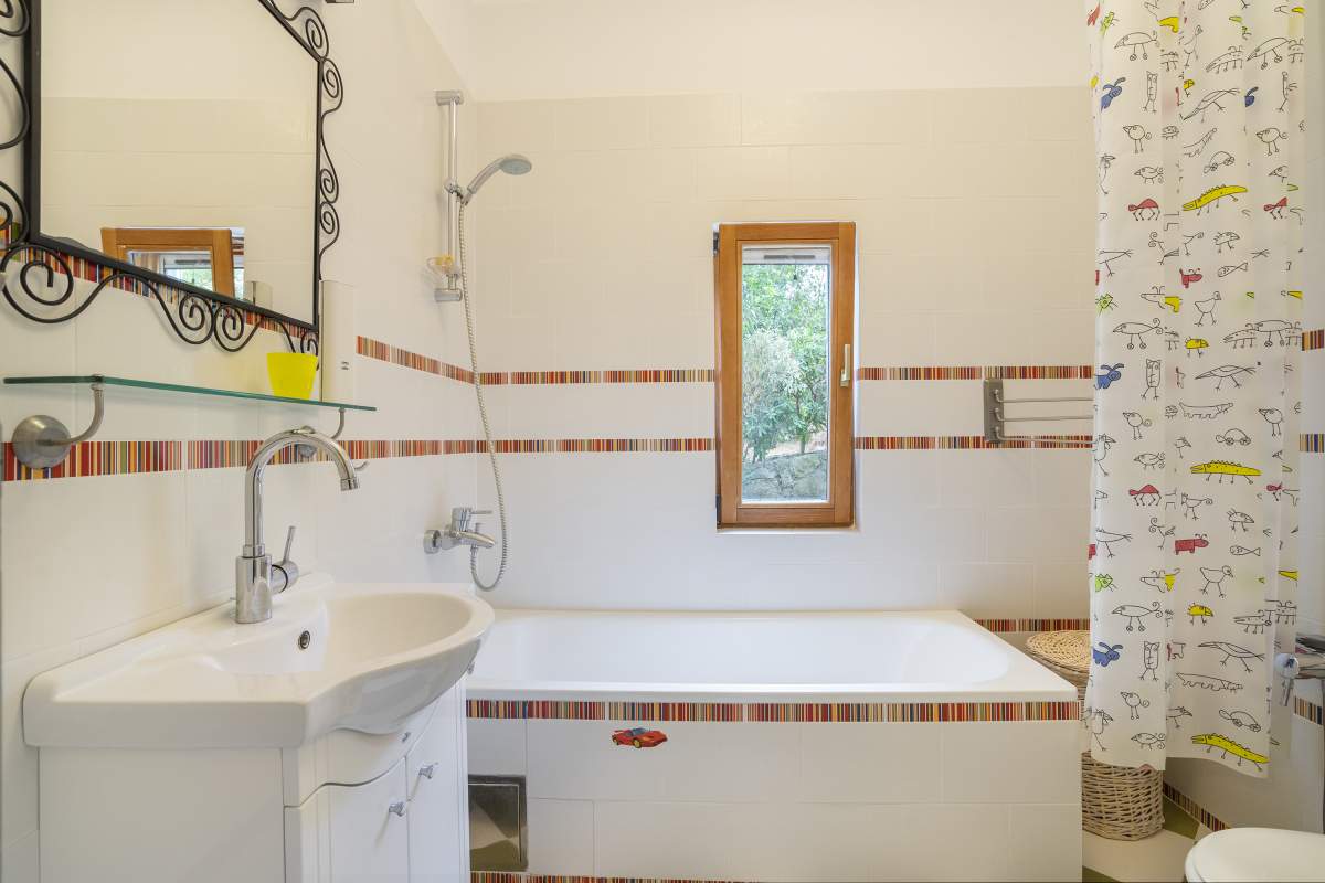 Badezimmer mit Badewanne und Fenster in einer Villa, Bigovo, Montenegro: helle Fliesen, geschmiedeter Spiegel und bunte Duschvorhang.