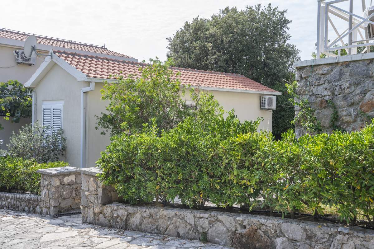 Fassade der Villa in Bigovo, Montenegro: Steinmauer, grüner Garten und eingeschossiges Haus mit Ziegeldach.