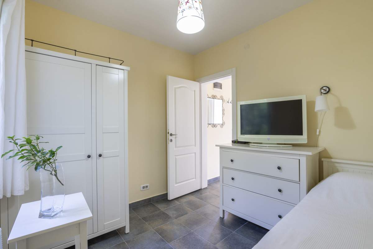 Helles Schlafzimmer mit weißen Möbeln und TV in einer Villa, Bigovo, Montenegro. Fliesenboden, gemütliches Interieur zum Entspannen.