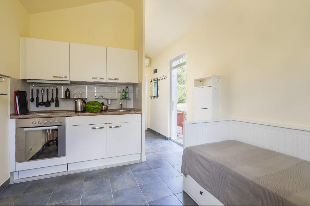 Studio-Küche mit weißer Einbauküche und Bett in einer Villa in Bigovo, Montenegro: moderne Ausstattung und Zugang zur Terrasse.