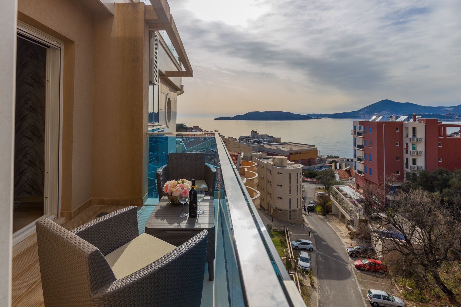 Penthouse balcony in Pržno, Montenegro: woven furniture, panoramic sea view and view of Sveti Stefan island.