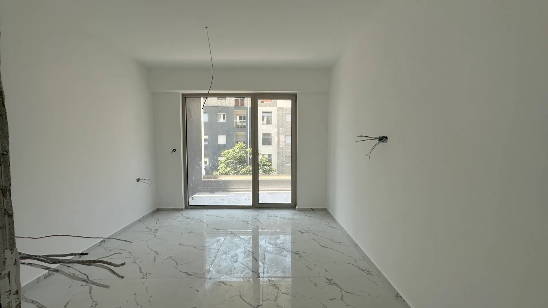 Wohnzimmer in einem Neubau in Budva, Montenegro: helle Ausstattung, Feinsteinzeugboden in Marmoroptik, Zugang zum Balkon.