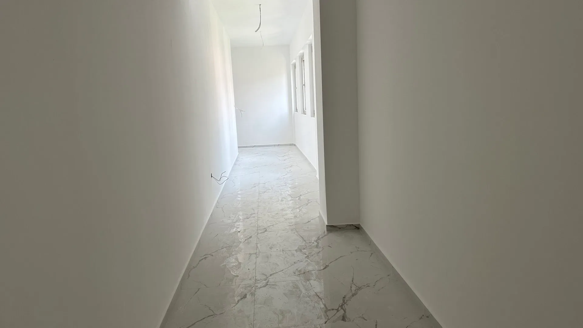 Heller Flur in einer neuen Wohnung in Budva, Montenegro: weiße Wände und ein Boden aus Feinsteinzeug in Marmoroptik, im Rohbauzustand.