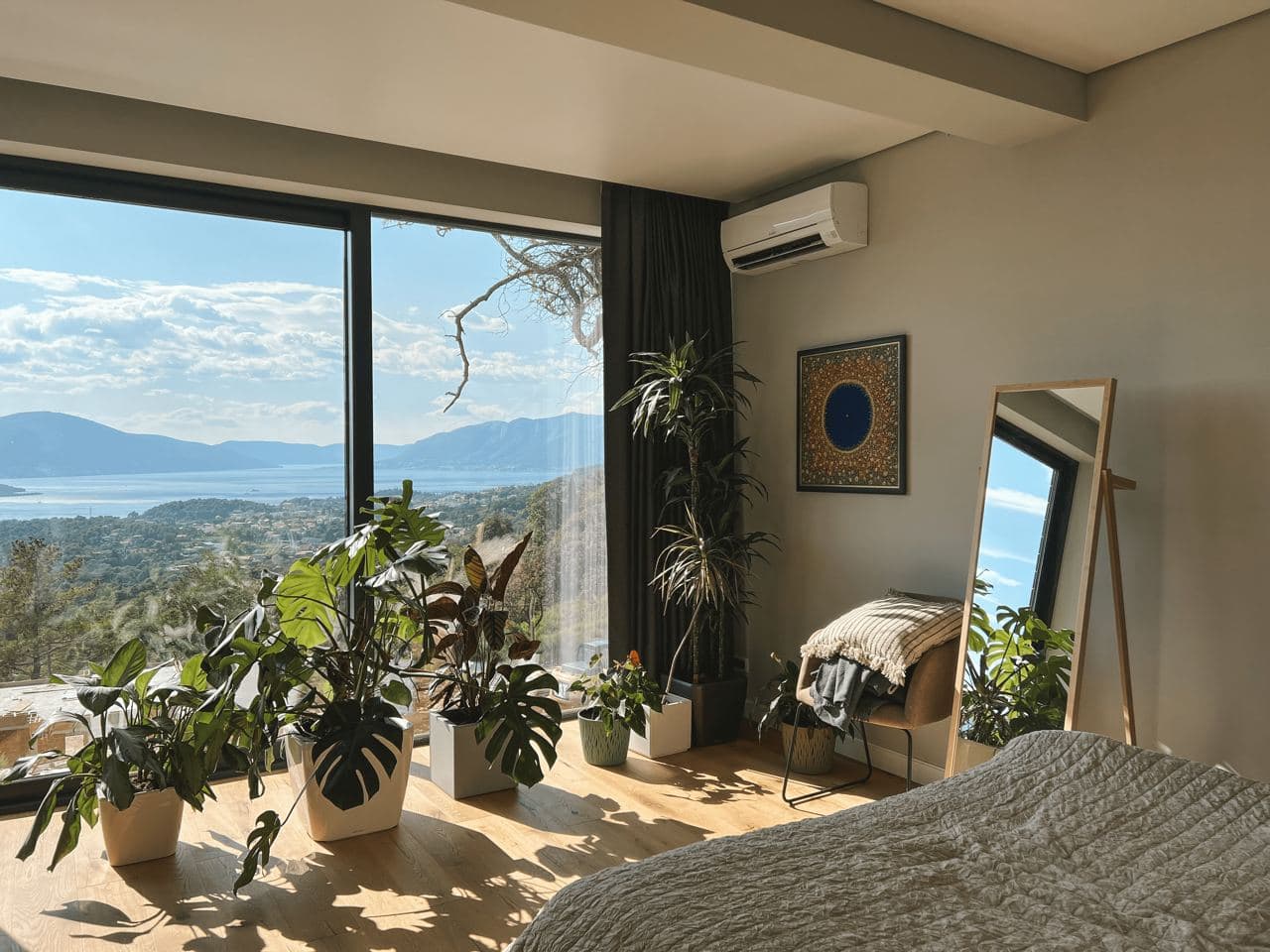 Schlafzimmer mit Panoramablick auf das Meer und die Berge in der Wohnanlage Kavac, Montenegro: stilvolles Interieur, viele Pflanzen und ein Standspiegel