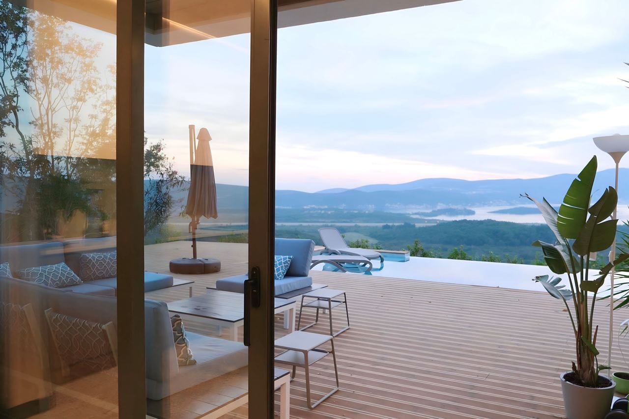 Terrasse mit Pool und Panoramablick auf die Berge in der Wohnanlage Kavac, Montenegro: moderne Möbel, Holzdeck und Sonnenliegen.