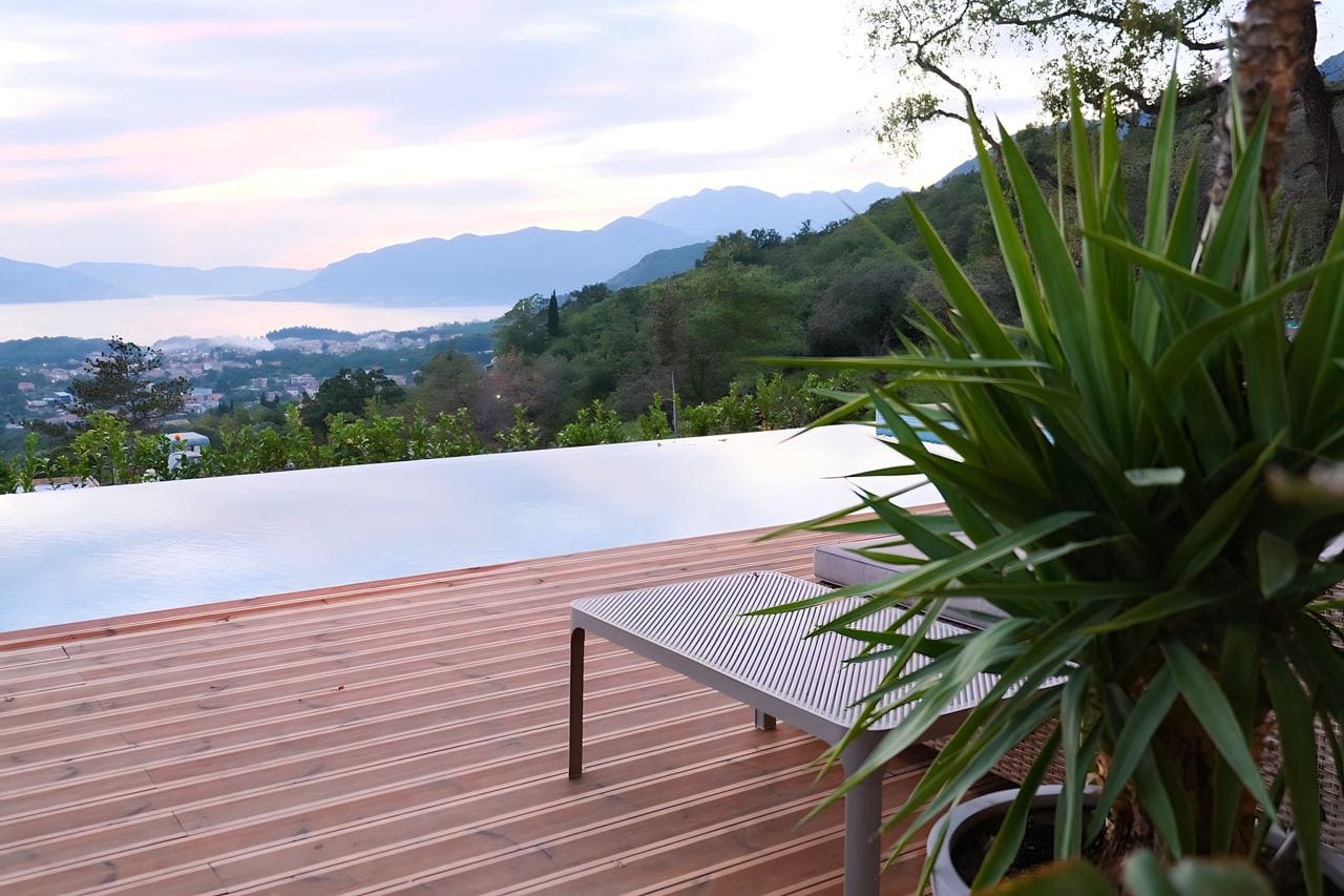 Infinity-Pool mit Terrasse und Meerblick in der Wohnanlage Kavac, Montenegro: Holzdeck und Liegestühle am Wasser.