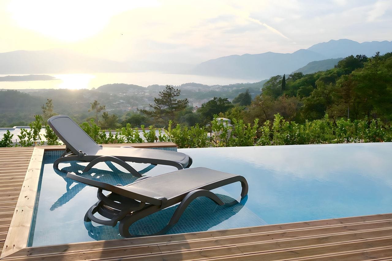 Infinity-Pool mit Liegen in der Wohnanlage Kavac, Montenegro: Panoramablick auf Berge und Bucht bei Sonnenuntergang.