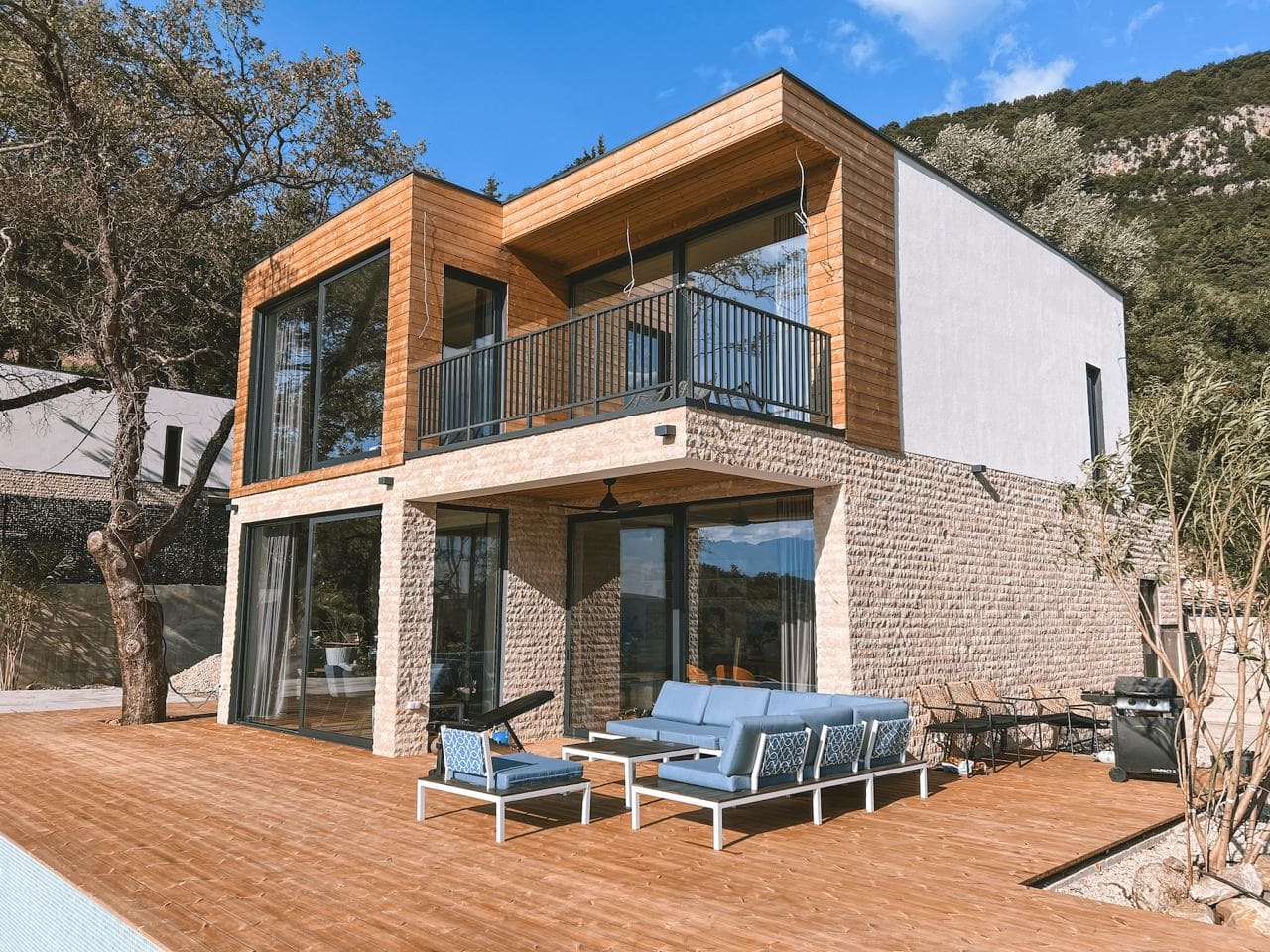 Moderne Villa in Kavac, Montenegro: zweistöckiges Haus mit Steinverkleidung, Terrasse, Möbeln und Panoramafenstern.