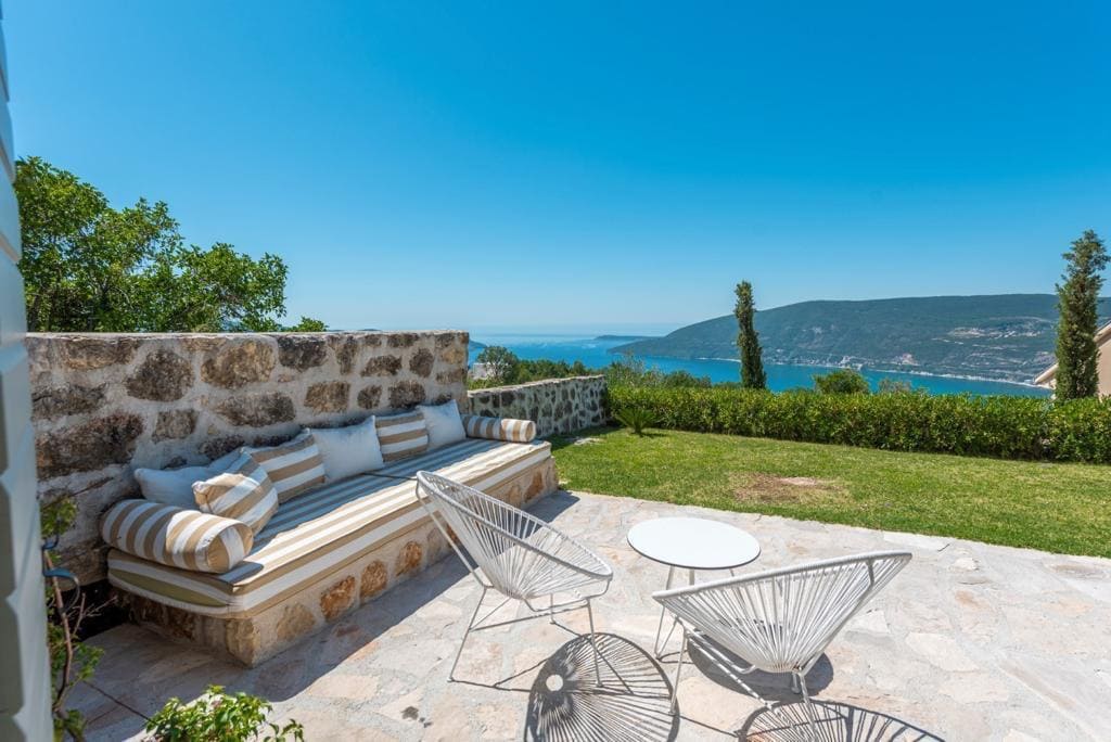 Terrasse de la villa à Herceg Novi, Monténégro : banc en pierre, fauteuils en osier et vue panoramique sur la mer Adriatique.