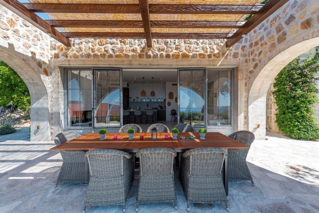 Terrasse de la villa à Herceg Novi, Monténégro : finition en pierre, mobilier en osier et vue sur la cuisine moderne à travers la baie vitrée.
