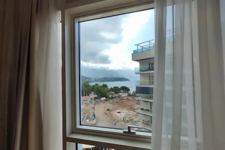 Blick aus dem Schlafzimmerfenster auf das Meer und die Stadt in einer Wohnung in Budva, Montenegro: moderne Apartments mit Panoramaverglasung.