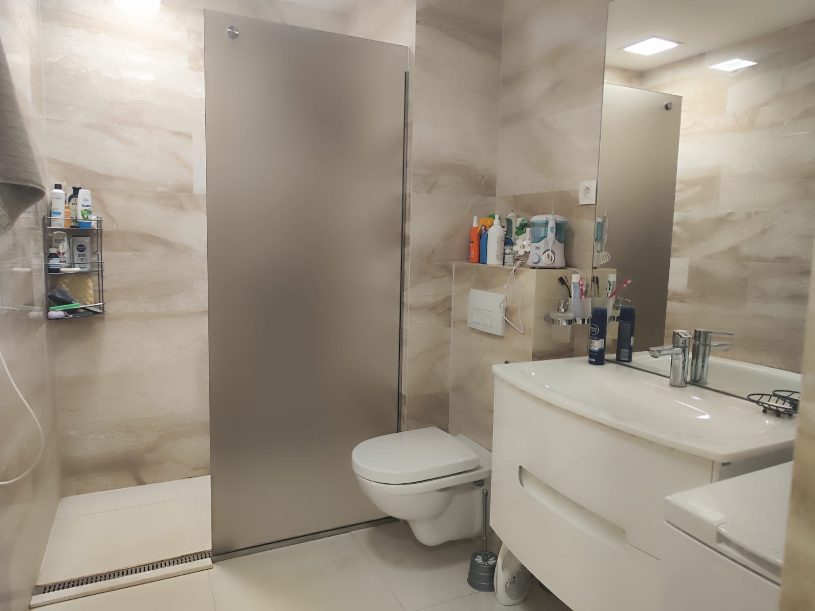 Modernes Badezimmer in einer Wohnung in Budva, Montenegro: Duschkabine, wandhängendes WC und weiße Waschtischkonsole mit Waschbecken.
