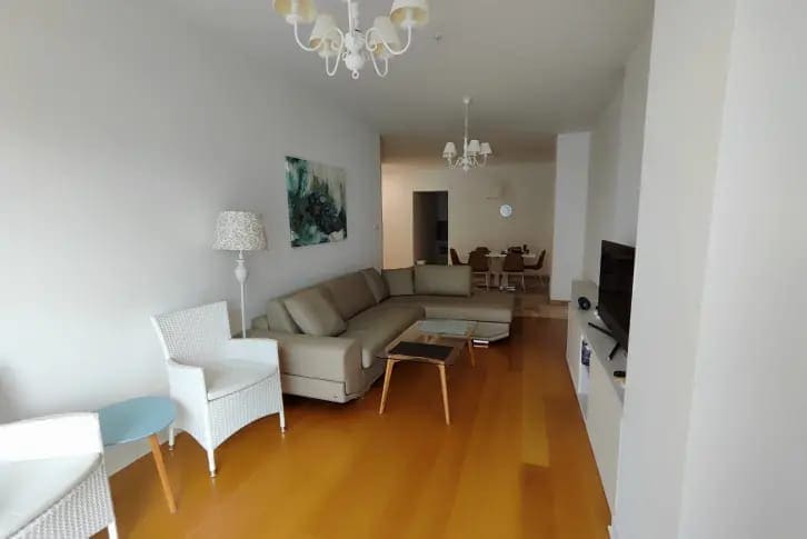 Geräumiges Wohnzimmer mit beigem Sofa und Essbereich in einer Wohnung in Budva, Montenegro, mit Parkettboden.