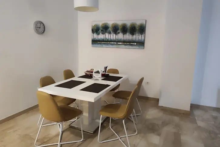 Heller Essbereich in einer Wohnung in Budva, Montenegro: weißer Tisch, senffarbene Stühle und ein Bild an der Wand.