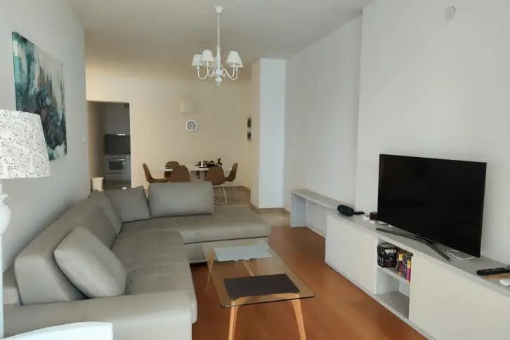 Helles Wohnzimmer mit grauem Ecksofa und Essbereich in einer Wohnung, Budva, Montenegro.