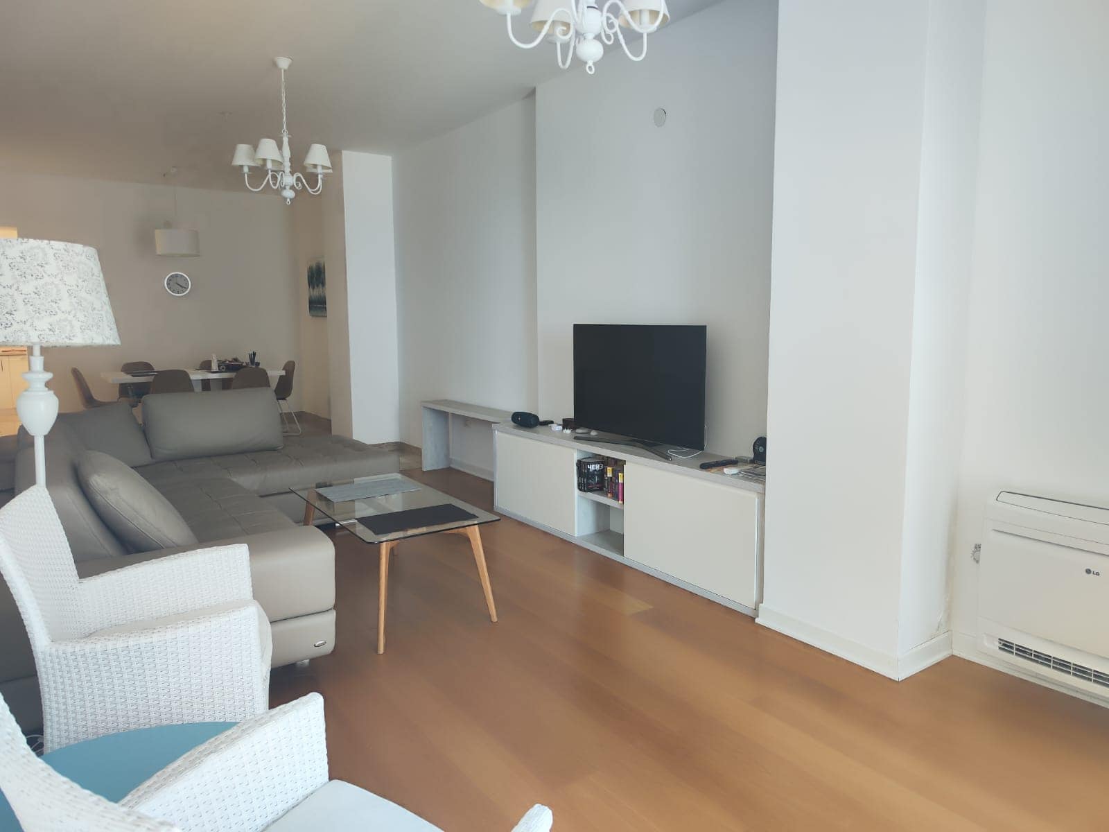 Helles Wohnzimmer in einer Wohnung in Budva, Montenegro: graues Ecksofa, TV-Bereich, Essgruppe und Parkettboden.