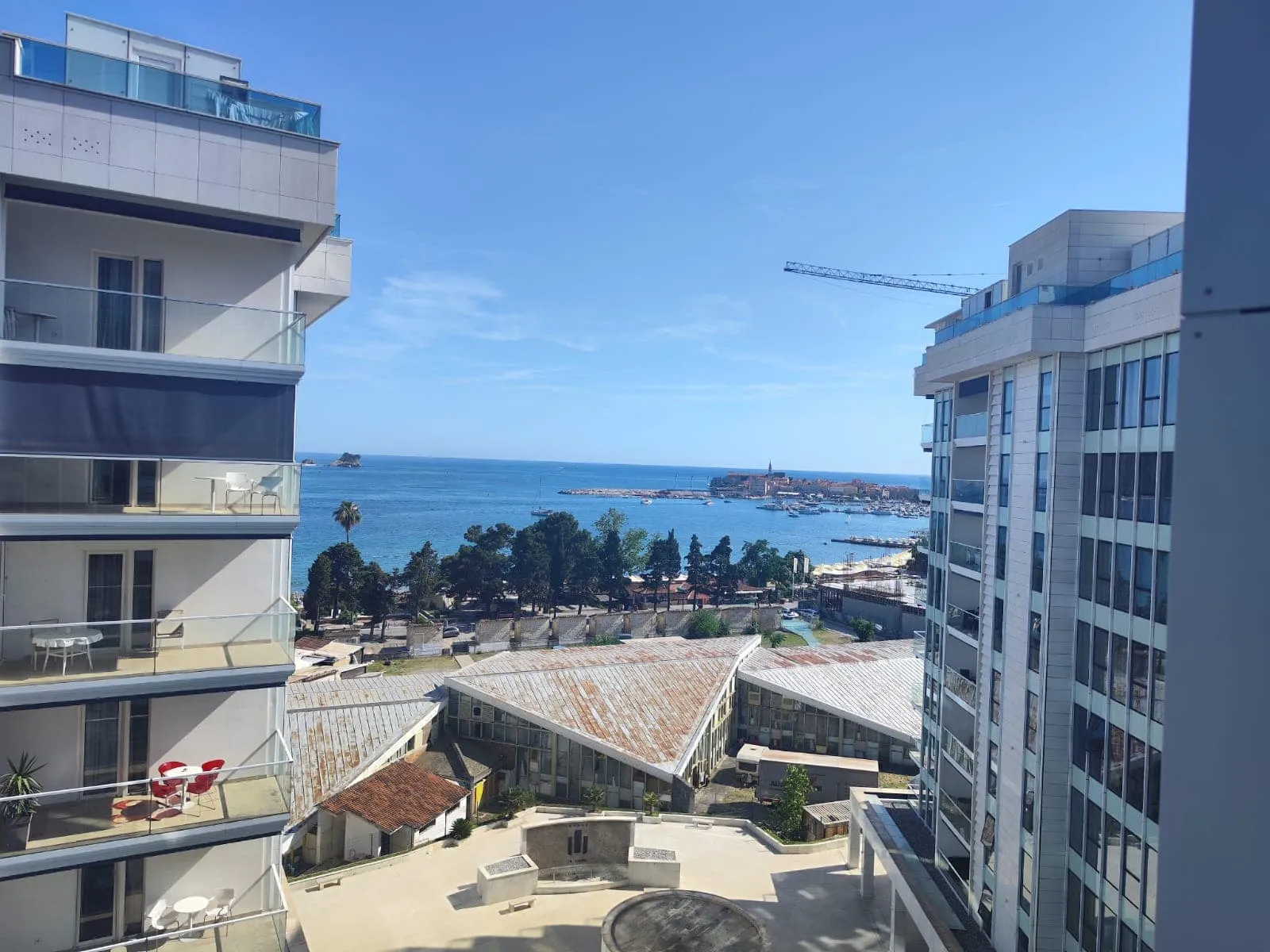 View from the balcony of a modern apartment in Budva, Montenegro: a panorama of the Adriatic Sea, the beach, and the cityscape.