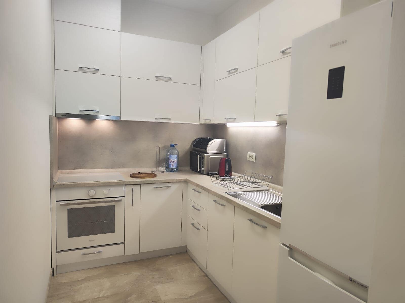 Moderne weiße Küche in einer Wohnung in Budva, Montenegro: Einbaugeräte, Schränke und Arbeitsflächenbeleuchtung.