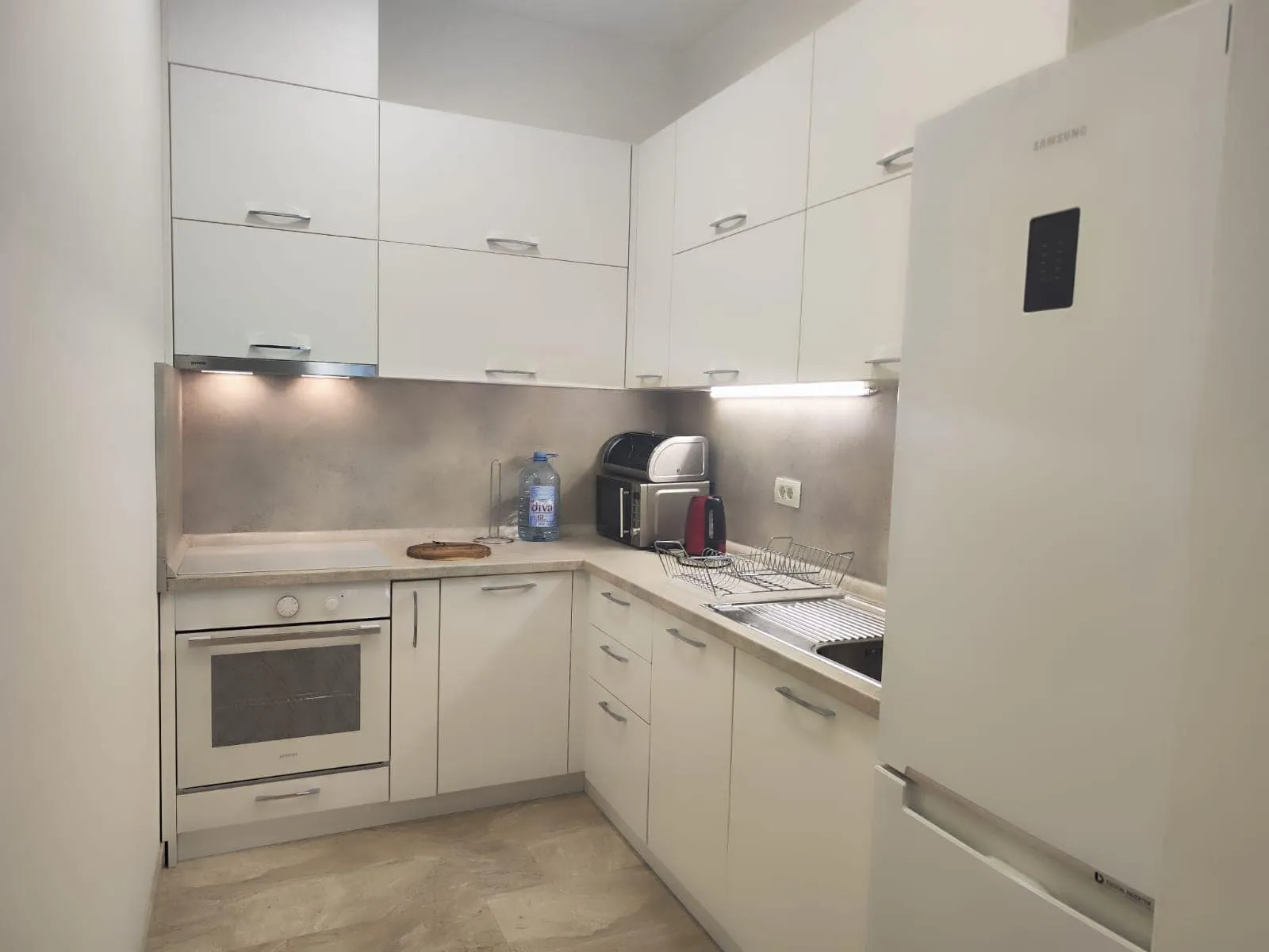 Modern white kitchen in an apartment in Budva, Montenegro: built-in appliances, cabinets, and under-cabinet lighting.