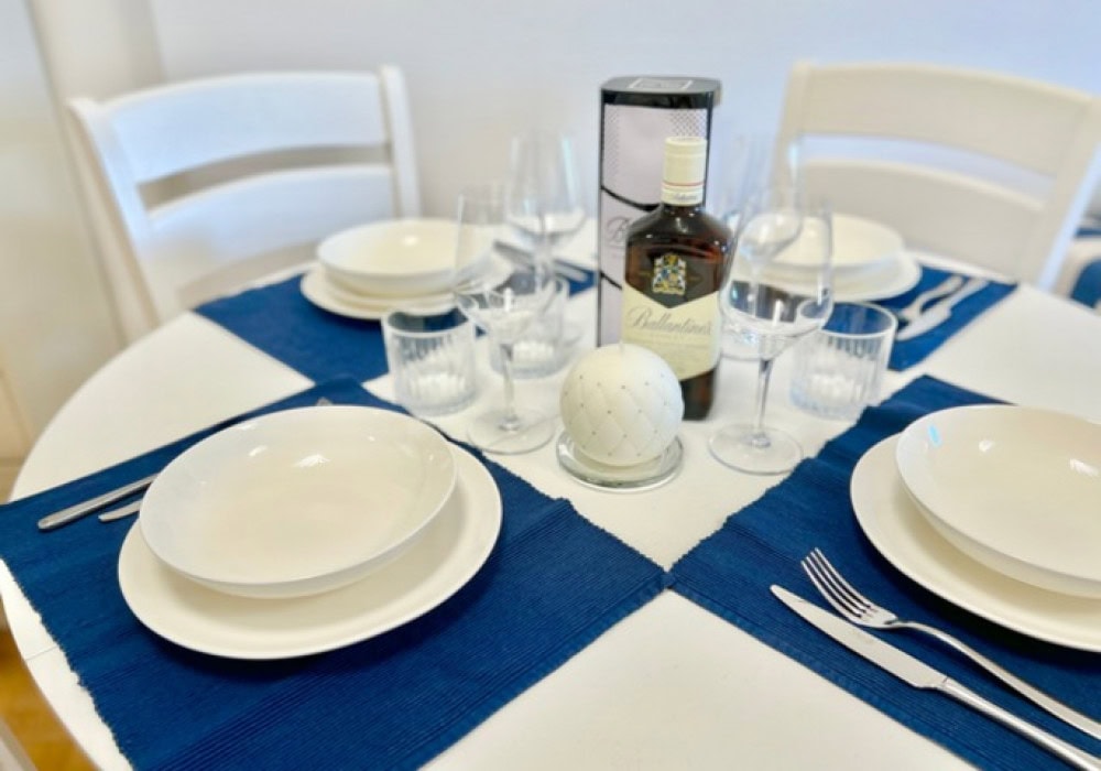 Gedeckter Esstisch im Wohnzimmer einer Wohnung in Bečići, Montenegro: weiße Möbel, blaue Servietten und Geschirr.