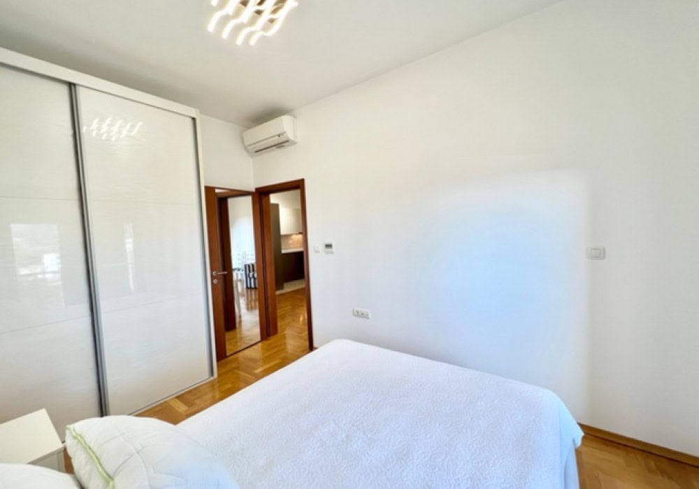 Helles Schlafzimmer mit weißem Schiebetürenschrank und Parkett in einer Wohnung in Bečići, Montenegro. Blick auf den Durchgang zur Küche.